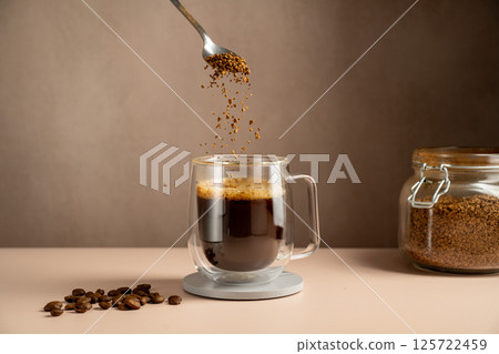 Instant coffee pouring in transparent glass mug, roasted coffee beans 125722459