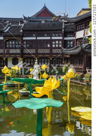 Shanghai, China - 1 April 2025: Serene pond in Yuyuan Garden with water lilies, golden fish, and a traditional statue. Historic Chinese architecture reflects in calm water. Peaceful cultural scene 125722583