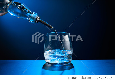 Vodka pours from bottle to glass with ice. 125723207