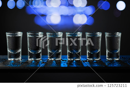 Alcoholic shots of tequila or strong drink in small wet glasses on a black table. 125723211