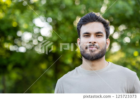 Portrait of a confident man with beard standing in park. Green trees in background highlight serene outdoor environment. Natural lighting offers vibrant and fresh feel. Portrait of a confident man with beard standing in park. Green trees in background highlight serene outdoor environment. Natural lighting offers vibrant and fresh feel. 125723373