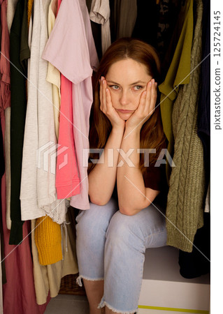 Woman can't decide what to wear, closet with too many clothing. Overburdened with clothes 125724145