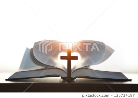 A cross symbolizing the death and resurrection of Jesus and a brightly lit heart-shaped Bible, the love of Jesus Christ in the background A cross symbolizing the death and resurrection of Jesus and a brightly lit heart-shaped Bible, the love of Jesus Christ in the background 125724197