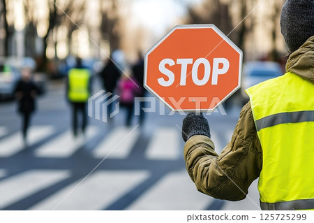 Traffic guard wearing yellow vest and holding stop sign 125725299