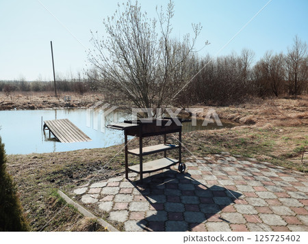 An Outdoor Barbecue Setup by a Tranquil Pond Creates an Idyllic Scene for Relaxation 125725402
