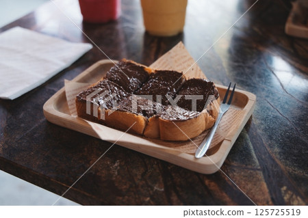 Enjoy a Delicious Slice of Toast Topped with Creamy Chocolate Spread on a Rustic Wooden Tray Enjoy a Delicious Slice of Toast Topped with Creamy Chocolate Spread on a Rustic Wooden Tray 125725519