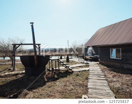 A picturesque rustic country scene featuring a traditional well and a charming house nearby A picturesque rustic country scene featuring a traditional well and a charming house nearby 125725817