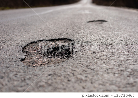 A damaged section of the highway shows cracks and holes, indicating the need for urgent repairs and maintenance to ensure driver safety 125726465