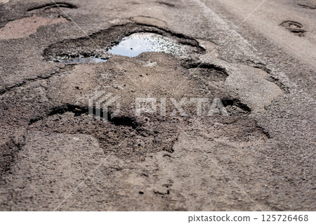 Cracked and broken asphalt on a highway displays large potholes, posing danger to vehicles and necessitating immediate repairs to ensure safety Cracked and broken asphalt on a highway displays large potholes, posing danger to vehicles and necessitating immediate repairs to ensure safety 125726468