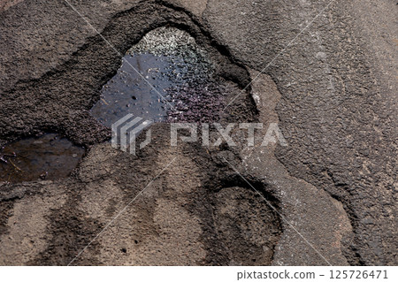 A cracked asphalt section shows a dangerous water-collecting hole, emphasizing the urgent need for traffic safety maintenance 125726471