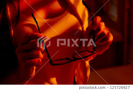 Closeup of Woman Holding Eyeglasses in Warm Sunset Office Light. 125726927