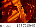 Woman Holding Eyeglasses in Golden Hour Office Light. 125726945