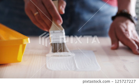 Repairman With A Paintbrush And White Paint Painting The Wooden Surface Of The Table Repairman With A Paintbrush And White Paint Painting The Wooden Surface Of The Table 125727227