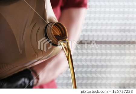 Mechanic With Canister Of Motor Oil Pouring From It Mechanic With Canister Of Motor Oil Pouring From It 125727228