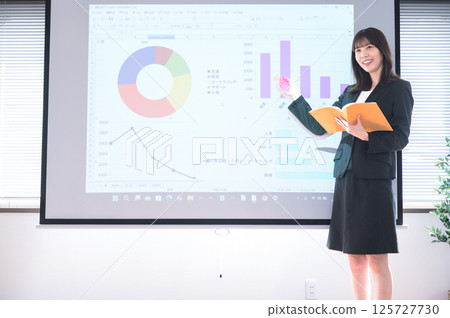 一位身穿西裝的年輕女子在投影機前做演示 125727730