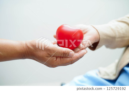 Asian elder senior woman patient holding red heart in hospital. 125729192