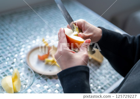 A woman carefully peeling an apple with a knife on a plate 125729227