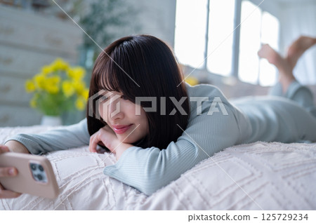 一位年輕女子的側面像，她輕輕地微笑著，手裡拿著一部智慧型手機 125729234