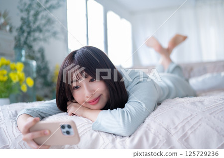 Relaxed young woman concentrating on the screen with her face resting on the pillow Relaxed young woman concentrating on the screen with her face resting on the pillow 125729236