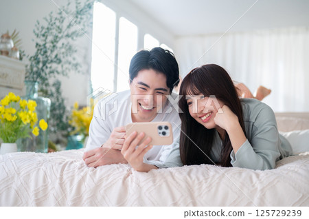 一對男女並肩坐在床上,享受著智慧型手機螢幕的幸福時光 一對男女並肩坐在床上,享受著智慧型手機螢幕的幸福時光 125729239