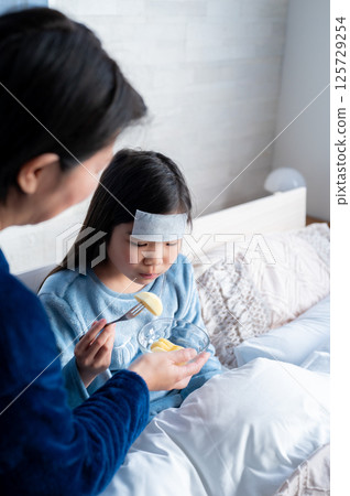 A mother's tender expression as she feeds her sick daughter A mother's tender expression as she feeds her sick daughter 125729254