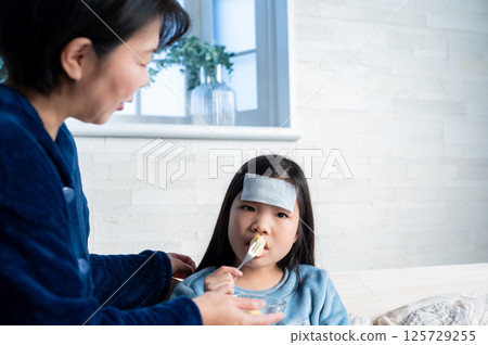 A child recuperating in bed with a cooling sheet on his forehead 125729255
