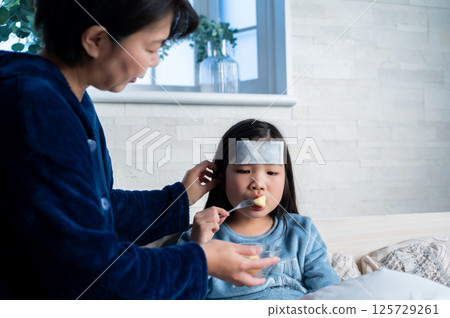 A mother's tender moment as she spoon-feeds her sick daughter porridge 125729261