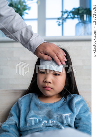 一位父親在室內輕輕地將手放在女兒的額頭上測量她的體溫 125729263