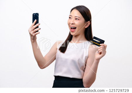 A beautiful young Asian businesswoman holds a credit card and a smartphone in her hand 125729729
