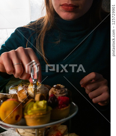 Woman Choosing a Mini Tart from a Tiered Stand 125729901