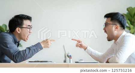 Two men arguing at desk, both pointing and shouting, intense expression, modern office setting 125731216