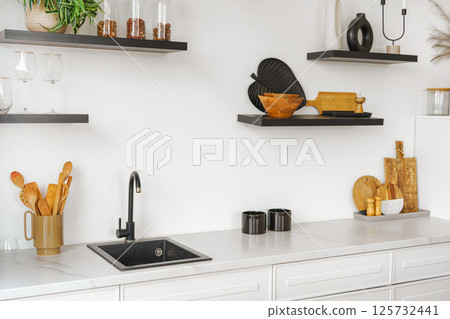 Kitchen interior with countertop and black water tap on white wall background with wooden shelves 125732441