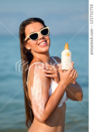 Beautiful Woman in Bikini Applying Sun Cream on Tanned Shoulder. Sun Protection. Skin and Body Care Concept. Girl Using Sunscreen.  Portrait Of Female Holding Suntan Lotion or Moisturizing Sunblock. 125732758