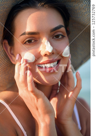 Woman smile applying sun cream on face. Skincare concept. Body Sun protection. sunscreen. Female in hat smear moisturizing lotion on skin. Woman smile applying sun cream on face. Skincare concept. Body Sun protection. sunscreen. Female in hat smear moisturizing lotion on skin. 125732769
