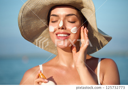 Beautiful Woman Face Portrait Beauty Skin Care Concept. Sunscreen. Suntan Lotion. Female is Applying on Beautiful on Face. Sunscreen Solar Cream. Sun protection.The Girl Uses Moisturizer Sunblock. 125732773