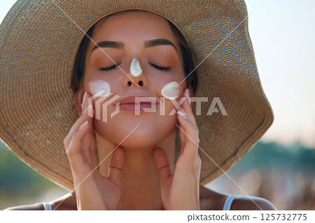 A woman smile applying sun cream on face. Skincare. Body Sun protection.  Female smear sunscreen moisturizing lotion on skin. Beauty skin care concept 125732775