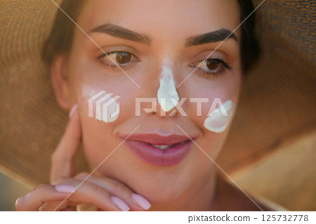 A woman smile applying sun cream on face. Skincare. Body Sun protection. Female smear sunscreen moisturizing lotion on skin. Beauty skin care concept A woman smile applying sun cream on face. Skincare. Body Sun protection. Female smear sunscreen moisturizing lotion on skin. Beauty skin care concept 125732778