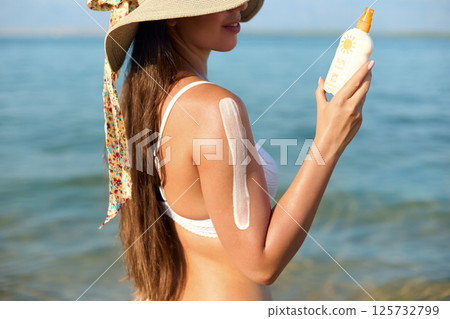 Beautiful Woman in Bikini Applying Sun Cream on Tanned Shoulder. Sun Protection. Skin and Body Care. Girl Using Sunscreen.  Portrait Of Female Holding Suntan Lotion 125732799