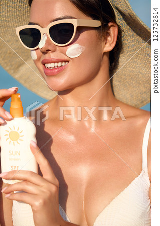 Beautiful young woman with sun cream on face. Girl holding sunscreen bottle on the beach and applying moisturizing lotion on skin.Skin care concept. Sun protection. Suntan. Beautiful young woman with sun cream on face. Girl holding sunscreen bottle on the beach and applying moisturizing lotion on skin.Skin care concept. Sun protection. Suntan. 125732814