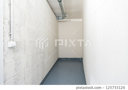 Small utility storage room with ventilation pipe and concrete walls Small utility storage room with ventilation pipe and concrete walls 125733120