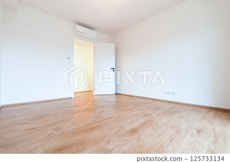 Bright and airy empty room in a contemporary apartment, featuring wooden flooring and white walls 125733134