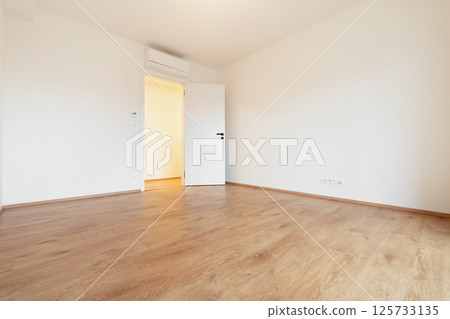 Modern and inviting empty apartment room with wooden floors, white walls, an air conditioning unit.  125733135