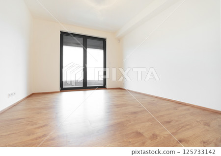 Minimalist empty room in a modern apartment with wooden floors and tilt and turn windows. 125733142