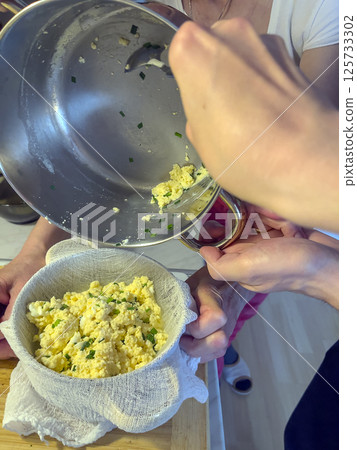 Women's hands prepare homemade cheese. The process of making homemade cheese with green onion feathers. Women's hands prepare homemade cheese. The process of making homemade cheese with green onion feathers. 125733302