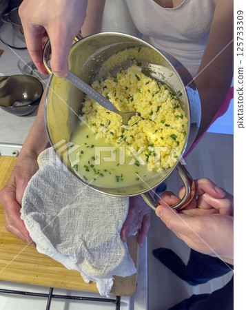 Process of making homemade cheese with green onion feathers. Women's hands prepare homemade cheese. 125733309