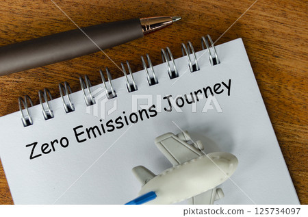 Top view of Zero Emission Journey text on white notepad with small airplane and pen background. Environmental awareness 125734097