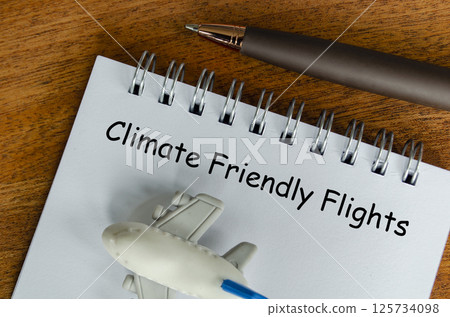 Top view of Climate Friendly Flight text on white notepad with small airplane and pen background. Environmental awareness 125734098