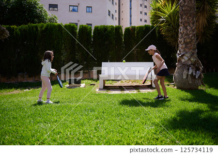 Two Girls Playing Paddle Tennis Outdoors in a Green Park Setting Two Girls Playing Paddle Tennis Outdoors in a Green Park Setting 125734119