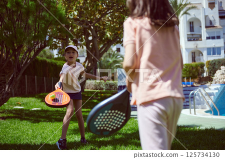Two Children Enjoying Paddle Tennis Outdoors in a Lush Green Park Setting 125734130