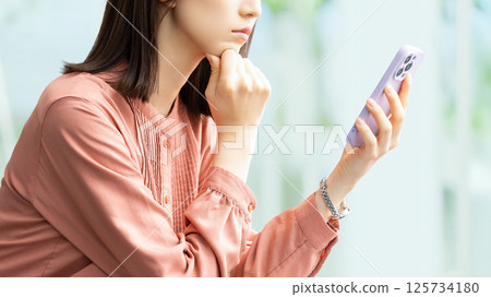 Woman/businesswoman thinking while looking at smartphone Woman/businesswoman thinking while looking at smartphone 125734180